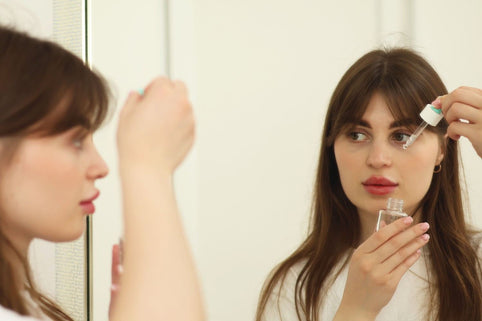 A young woman applying skincare serum in front of a mirror indoors