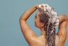 Woman with long hair washing it with shampoo against blue background